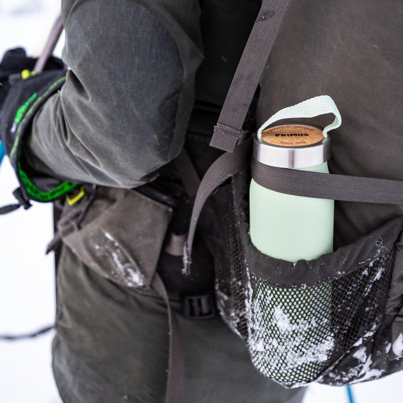 Person in winter gear with a backpack and water bottle in a snowy landscape